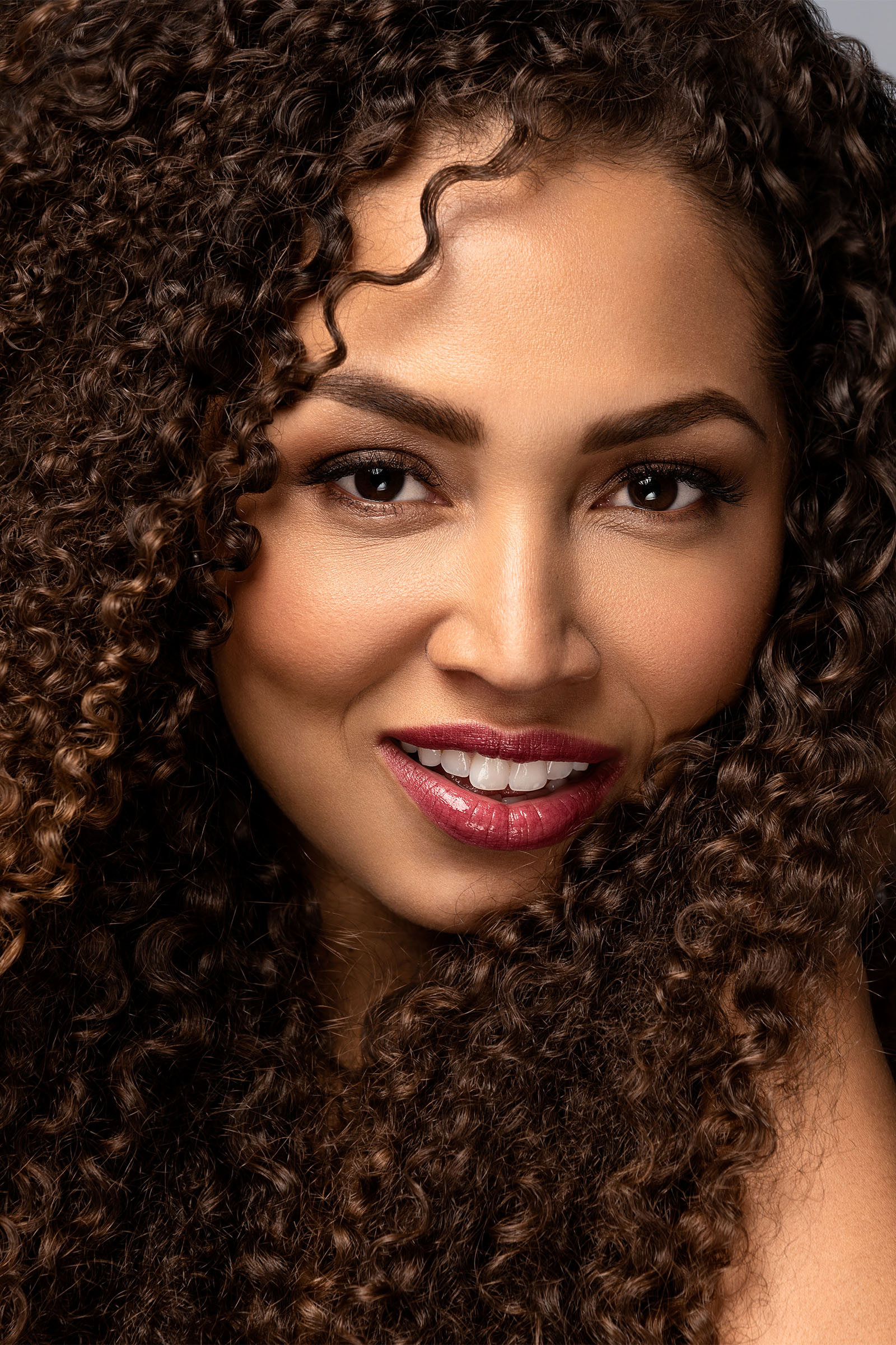 Female model closeup with long curly black ebony hair, smiling by Utah photographer Christopher Loke