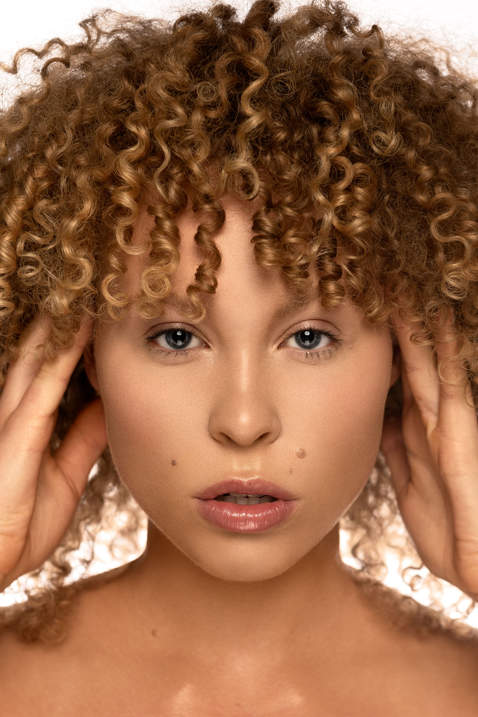 Closeup beauty shot of a female model with blonde curly hair looking straight at camera, subtle expression by Utah photographer Christopher Loke