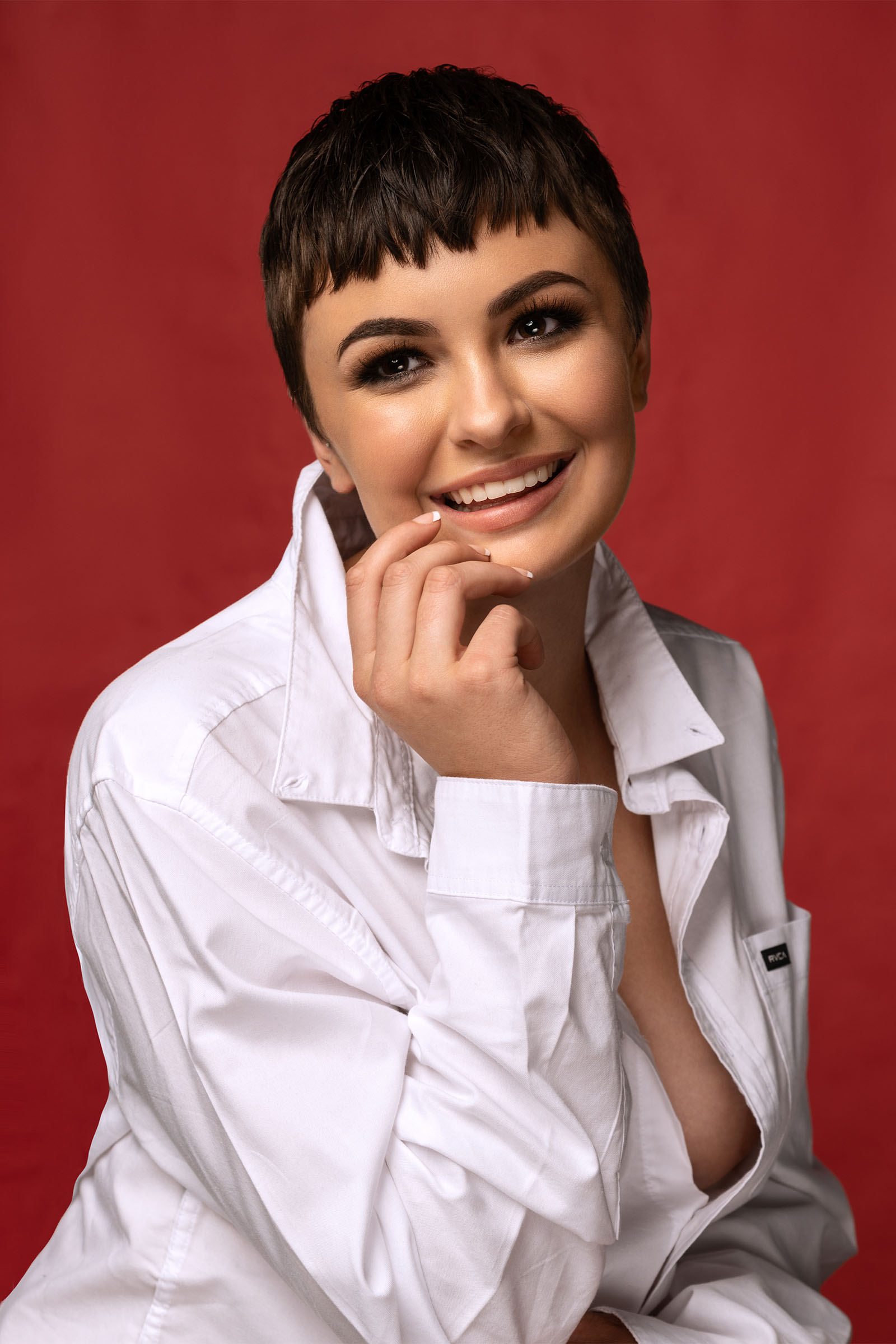 Beauty portrait of smiling female model, short modern pixie cut, white blouse, vermillion background by Utah photographer Christopher Loke