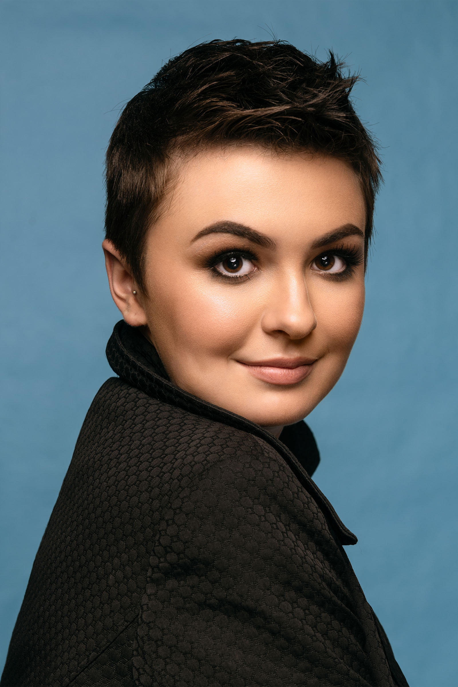 Beauty of female model, pixie haircut, blue background, giving us a shoulder, big, bright eyes, impeccable makeup by Utah photographer Christopher Loke
